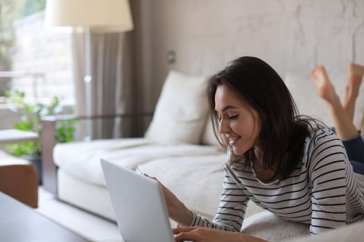 Happy natural brunette using credit card and laptop in the living room