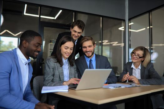 Group of happy diverse male and female business people in formal gathered around laptop computer in bright office