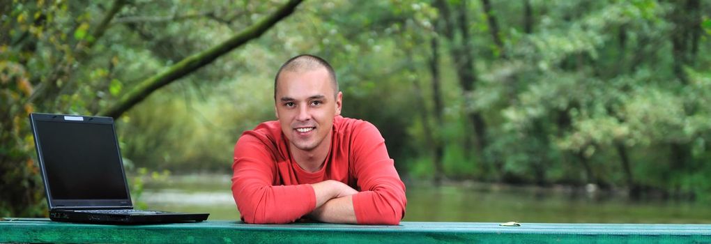 one young businessman working on laptop outdoor with green nature in background