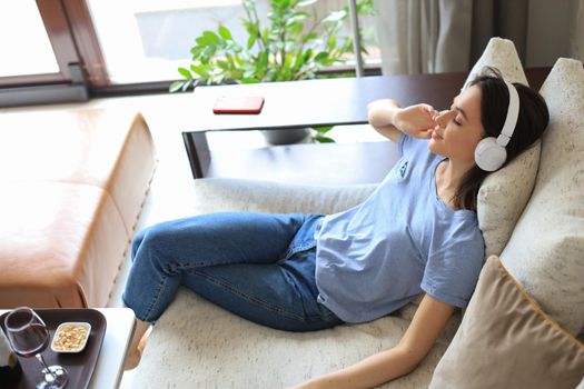 Beautiful brunette woman in earphones sitting on sofa listening to music with closed eyes