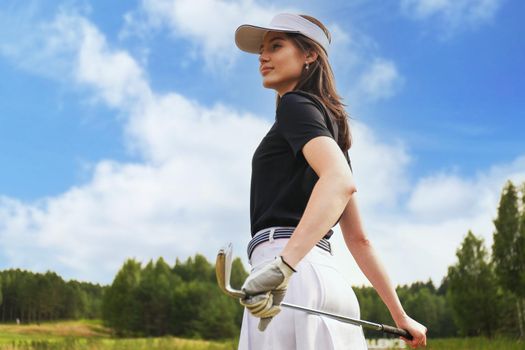 Professional female golfer holding golf club on field and looking away. Young woman standing on golf course on a sunny day.