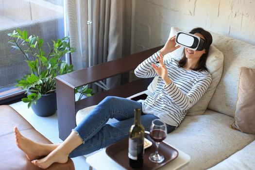 Young casual girl wearing VR headset while lounging on couch at home and looking around