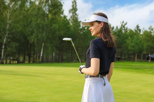 Professional female golfer holding golf club on field and looking away. Young woman standing on golf course on a sunny day.