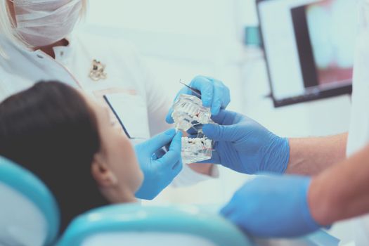 Senior male dentist in dental office talking with female patient and preparing for treatment.