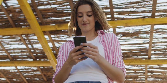 young woman using mobile cell smart phone app at beach during sunset on autumn day