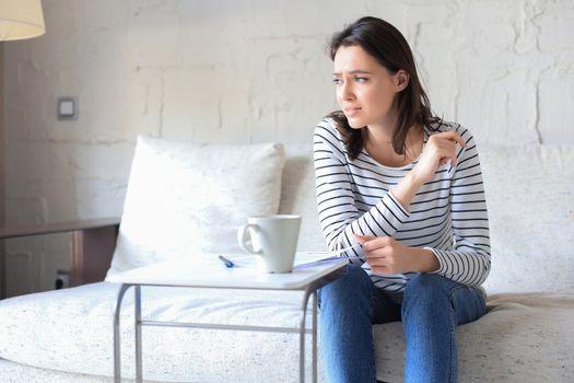 Sad woman with the bills sitting on a sofa in the living room
