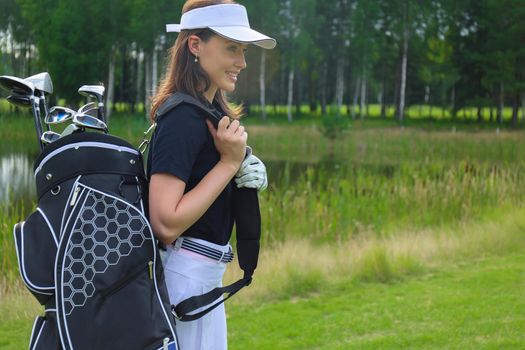 Beautiful golf woman player carrying a golf bag and smiling
