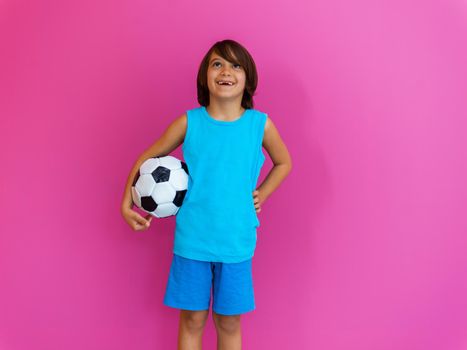 Portrait of young Arabic boy with soccer ball isolated against a pink background and copy space. High quality photo