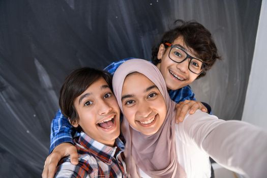 Group of Arab teens taking selfie photos on a smartphone with black chalkboard in the background. Selective focus. High quality photo