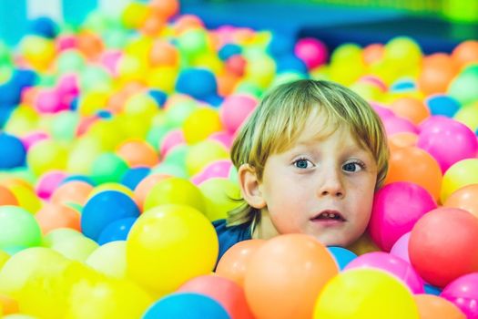 Happy little kid boy playing at colorful plastic balls playground high view. Funny child having fun indoors.