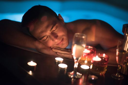 young handsome man enjoys relaxing in the jacuzzi with candles and champagne at luxury resort spa