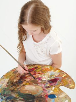 Cute little girl with a palette and a brush. The concept of children's creativity, learning to draw.