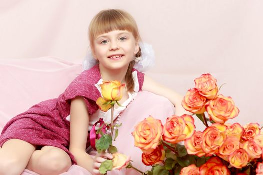 Beautiful little blonde girl with short bangs and pigtails on her head in a good mood.She hugs a bouquet of tea roses.