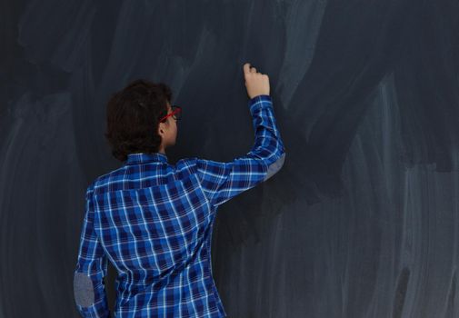 Smart  Arab Teen Boy with chalk in hand writing on empty black board in school