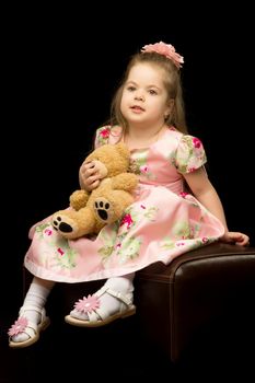 A nice little girl with a teddy bear. Studio photo on a black background. The concept of a happy childhood, publication on the cover of the magazine.