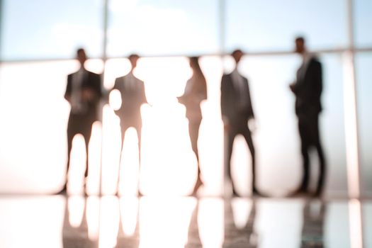 Silhouettes of businesspeople standing against panoramic office window