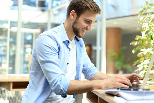 Portrait of young man sitting at his desk in the office and typing on the laptop