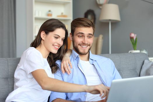 Young couple doing some online shopping at home, using a laptop on the sofa