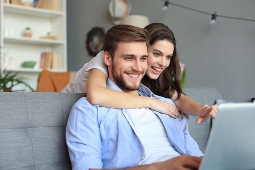 Young couple doing some online shopping at home, using a laptop on the sofa