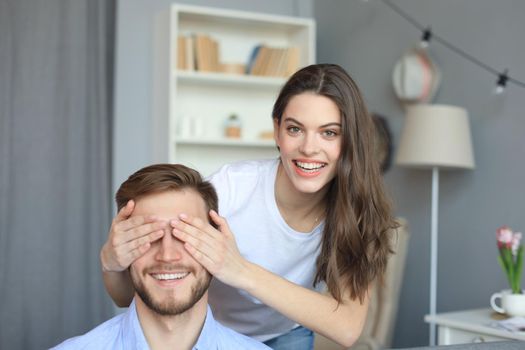 Young cute woman covering her husband's eyes