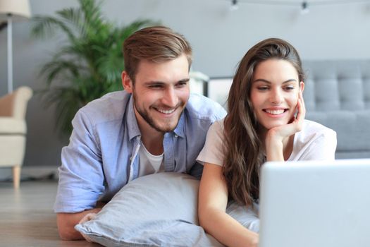 Young couple doing some online shopping at home, using a laptop on floor