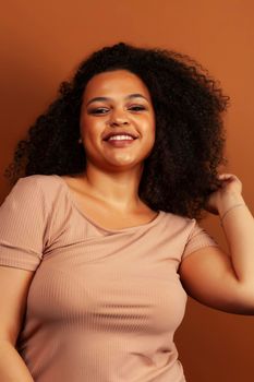 pretty young african american woman with curly hair posing cheerful gesturing on brown background, lifestyle people concept close up