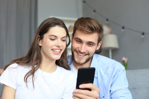 Young couple watching online content in a smart phone sitting on a sofa at home in the living room