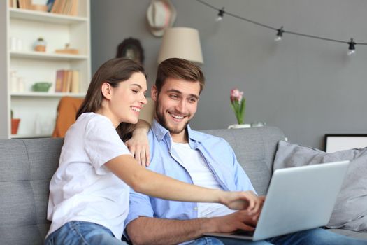 Young couple doing some online shopping at home, using a laptop on the sofa