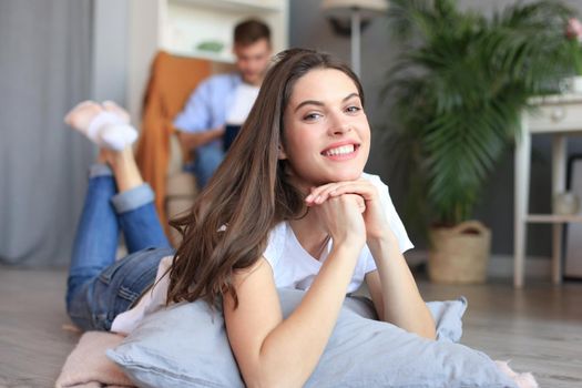 Portrait of attractive woman relaxing on floor with blurred man in background