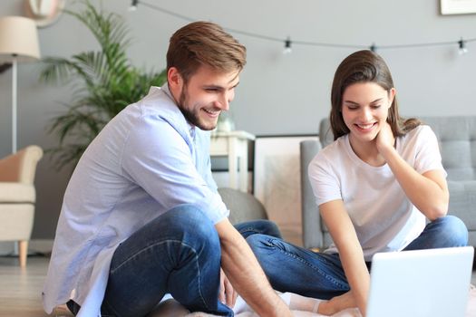 Young couple doing some online shopping at home, using a laptop on floor