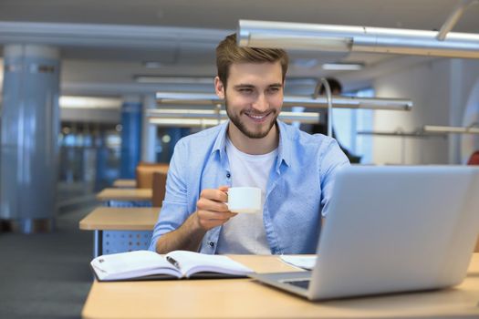 young man drinking coffee in office while typing on laptop