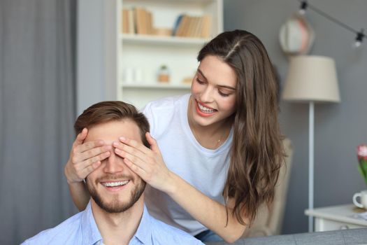 Young cute woman covering her husband's eyes