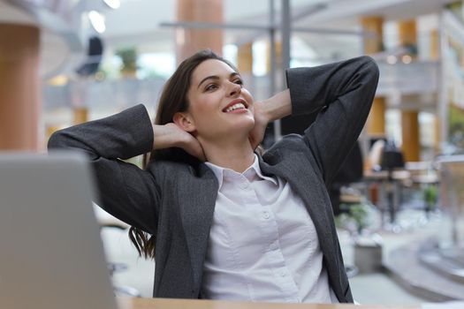 Young businesswoman sitting at office desk hold hands behind head relaxing feels good