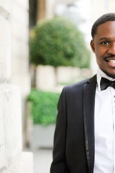 Portrait of afro american smiling man wearing dark suit and standing outdoors. Concept of black businessman.