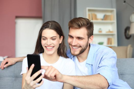 Young couple watching online content in a smart phone sitting on a sofa at home in the living room