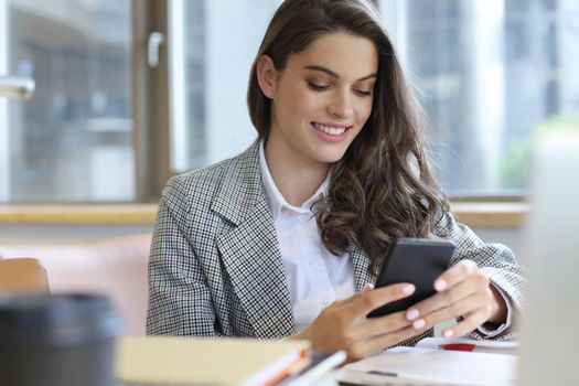 Young smiling business woman using smartphone near computer in office