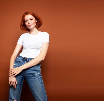young pretty redhead girl posing cheerful on warm brown background, lifestyle people concept close up