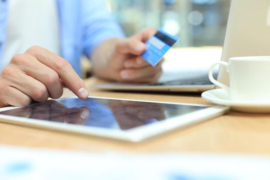 Young man sitting in office and pays by credit card with his tablet