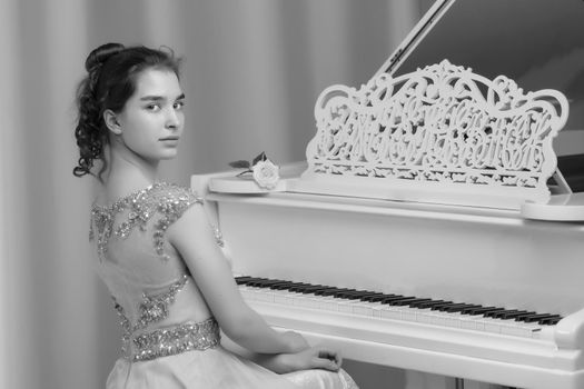 A teenage girl is playing on a white grand piano. The concept of creative development of personality, music education.
