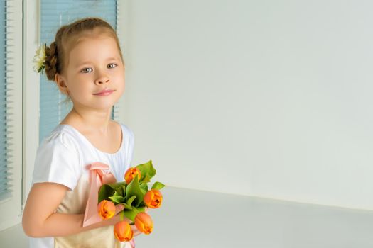 A nice little girl sits on a window sill with a bouquet of tulips. The concept of happy people, spring vacation.