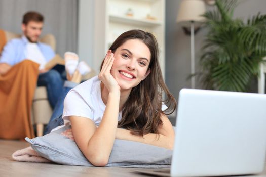 Smiling beautiful woman using laptop with blurred man in background at home