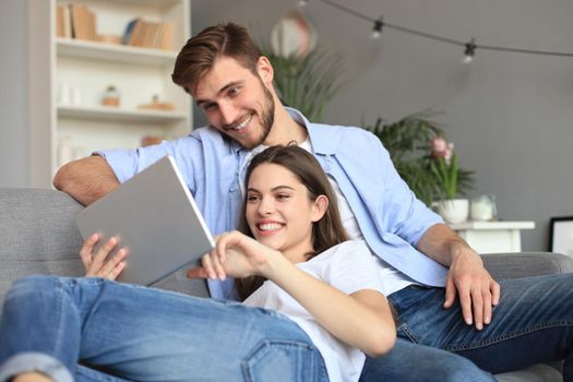 Young couple watching media content online in a tablet sitting on a sofa in the living room