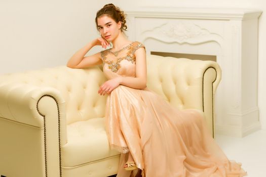 Beautiful teen girl very beautiful, smart dress sitting on the couch. The concept of style and fashion.