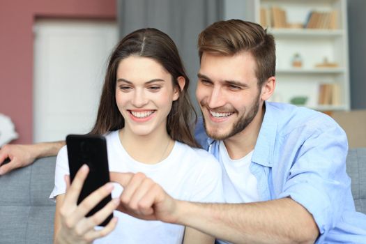 Young couple watching online content in a smart phone sitting on a sofa at home in the living room