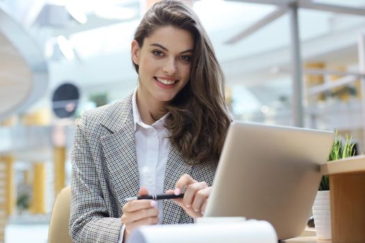 Portrait of a cheerful young businesswoman sitting at the table in office and looking at camera