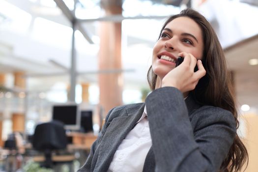 Young smiling business woman using smartphone near computer in office