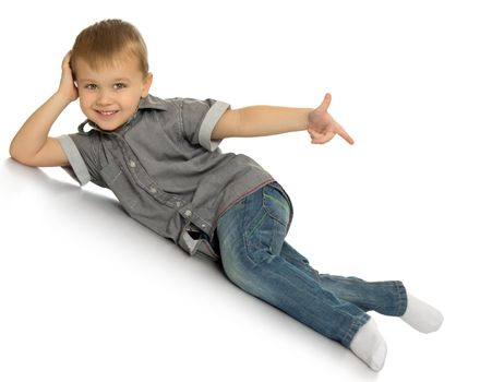 Laughing little boy in jeans and a gray shirt. The boy lies on the floor at an angle and points the index finger in the direction - Isolated on white background