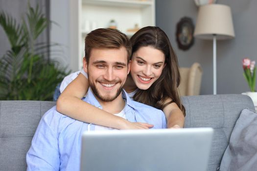 Young couple doing some online shopping at home, using a laptop on the sofa