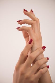 closeup of hands of a young woman with long red manicure on nails against white background