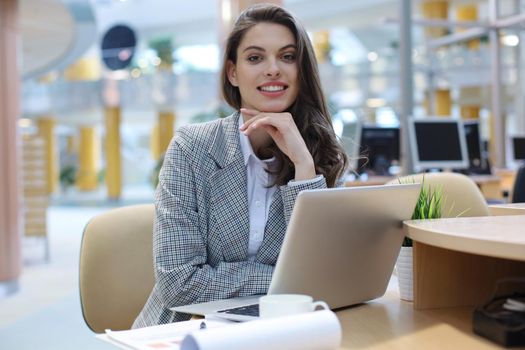Portrait of a cheerful young businesswoman sitting at the table in office and looking at camera